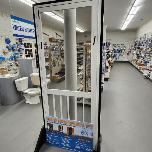 A screen door display stands in the center of a hardware store aisle. Surrounding shelves are stocked with plumbing supplies, creating a utilitarian ambiance.