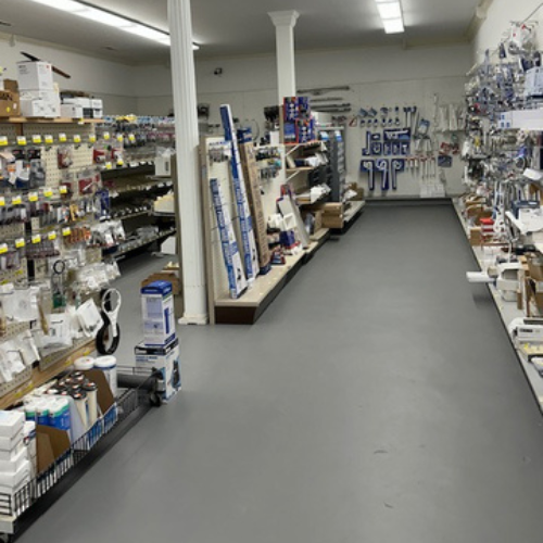 A hardware store aisle with neatly arranged shelves filled with tools, accessories, and supplies. Bright lighting creates a clean, organized atmosphere.