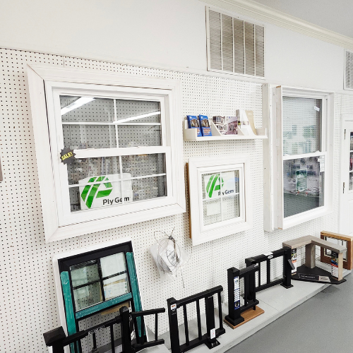 Display wall showcasing various Ply Gem windows with different designs and frames. Sample pieces and accessories are neatly arranged below. Bright showroom setting.